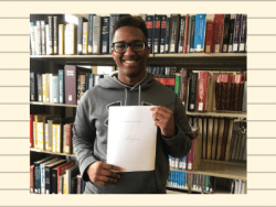 Student holding his award-winning paper in front of books